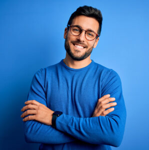 Caucasian male wearing blue shirt and glasses smiling standing in front of a blue background