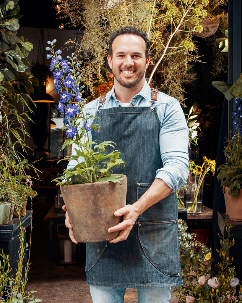 Caucasian male plant shop owner holding a plant and smiling at the camera