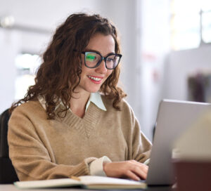 Caucasian female wearing glasses smiling at computer screen sitting at desk