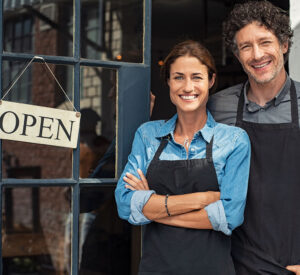 Caucasian couple standing at the front door of their business smiling